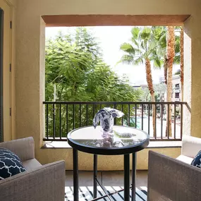 A balcony with a table and two chairs overlooking a lush green area.