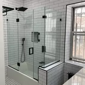 This custom-designed shower features sleek glass panels, matte black hardware, and classic white subway tile with bold black grout for a striking contrast. A built-in shower niche adds functionality, while a rainfall showerhead and handheld wand elevate the luxury. Finished with hexagonal mosaic flooring and abundant natural light, this bathroom renovation reflects Arber Construction Group’s modern craftsmanship and attention to every refined detail.