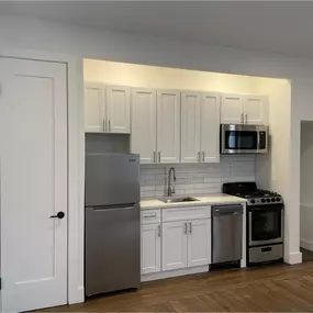 This space-maximizing kitchen remodel blends function and style, featuring shaker-style cabinetry, stainless steel appliances, and a classic white subway tile backsplash. The sleek under-mount sink, quartz countertops, and built-in microwave create a seamless, modern look ideal for urban living. Finished with warm wood flooring and recessed lighting, this project by Arber Construction Group delivers smart design in a small footprint — perfect for NYC apartments.