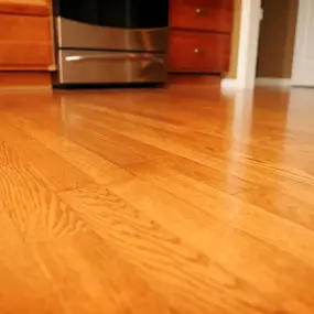 This image showcases a warm-toned, polished red oak hardwood floor. The flooring features a classic strip pattern and a glossy finish, reflecting light and highlighting the natural wood grain.