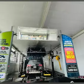 View from inside a car approaching the wash tunnel. The overhead signs clearly communicate wash tier options while showcasing modern brush equipment in action.