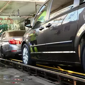 A staff member assisting customers in the tunnel during a premium Ceramic Shield wash. Includes safety signage, foam application, and lane control.
