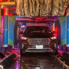A customer driving through the vibrant, high-tech tunnel at Olympic Speedwash in West LA. The advanced wash system uses colorful lights, soft-touch brushes, and efficient automation to deliver a deep clean in just minutes.
