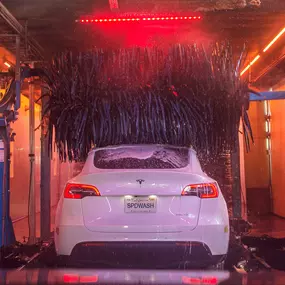 A white Tesla Model Y moves through the illuminated tunnel at Speedwash Northridge on Reseda Blvd, undergoing a premium ceramic wash with graphene protection. Vibrant lighting, branded signage, and soft-touch scrubbers highlight the express wash’s advanced vehicle care system. Clear instructional graphics—“Feet Off Pedals,” “Car in Neutral”—ensure a smooth and safe experience for all customers.