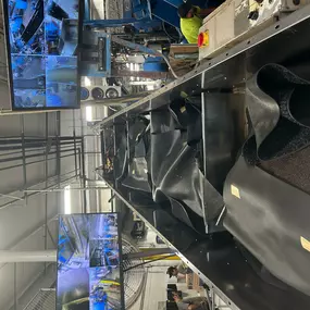 A conveyer belt in the Packerland warehouse moves mats down the line to be cleaned. Behind the conveyer belt system are two televisions with cameras showing different views of the warehouse.