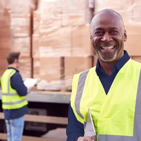 Smiling logistics worker holding a tablet in front of palletized boxes.