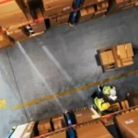 An overhead view of a warehouse with workers in safety vests handling boxes and pallets between tall storage racks.