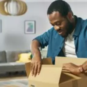 Man happily opening a package fulfilled by Valley Distribution and Logistics in his living room.