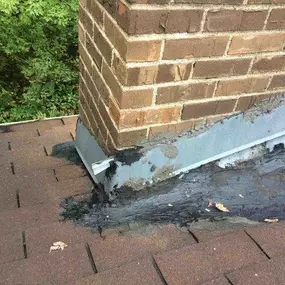 Roof repair in progress around a chimney base, highlighting damaged flashing and sealant areas.
