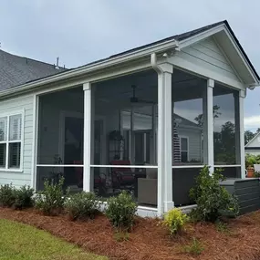 A modern two-story home with light green siding, dark trim, a two-car garage, and a brick foundation, surrounded by trees on a green lawn.