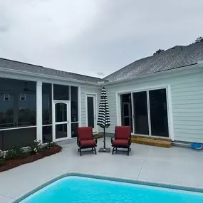 The back of a light-colored home with a covered patio, a small swimming pool, and an outdoor seating area under a black-and-white umbrella.