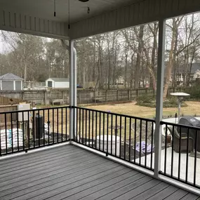 A spacious screened-in porch with a gray deck, black railing, and a view of a backyard with a pool, fence, and bare trees in winter.