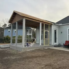 A spacious screened-in porch under construction, with a wood frame and new roof, attached to a home with light blue siding.