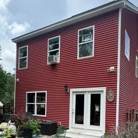 The back of a red-sided two-story home, with a small outdoor patio area, a metal table and chairs, and a sliding glass door.
