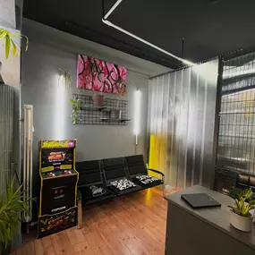 Warteraum mit schwarzen Sitzbänken farbigem Arcade Automat Pflanzen grauen Wänden und Kunstwerken im modernen Stil.