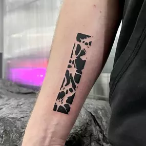 Rechteckiges Blackwork-Tattoo am Unterarm mit abstraktem Muster aus schwarzen Flächen.