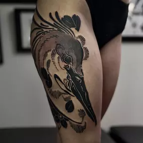 Blackwork-Tattoo eines abstrakten Reiherkopfes mit floralen Details auf dem Oberschenkel.