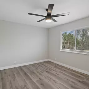 an empty bedroom with a window and a ceiling fan