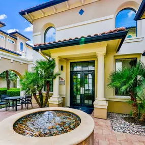 Paved walk way leading up to the leasing center, with a fountain and palm trees.