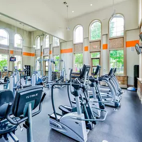 Fully equipped fitness center with cardio equipment, soaring windows, black flooring and tan walls