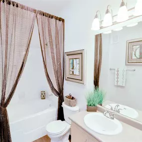 Spacious bathroom with tan counter top, white fixtures, large mirror, and brown shower curtain