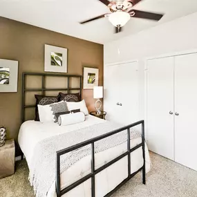 Expansive bedroom with beige carpet, white closets, a queen sized bed and a ceiling fan