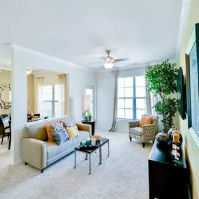 Large living room with cream carpeting, a beige couch, a tan chair and tall windows that provide natural light