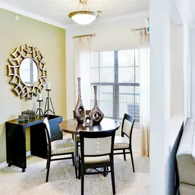 Interior dining room located next to tall windows, mirror, table and 4 tan chairs