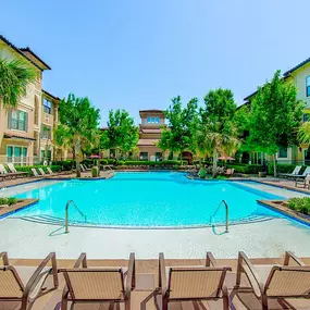 Outdoor pool with tan stone walkways and palm trees surrounding it