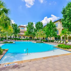 Large swimming pool surrounded by trees, tan stone, and white lounge chairs