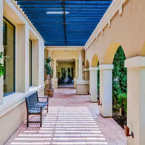 Exterior of apartment with paved walking paths, tan archways, and black bench