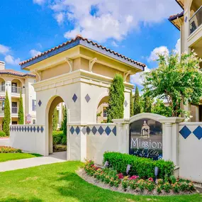 Exterior entrance to apartments with green lawns, floral beds, sign, and a paved walkway