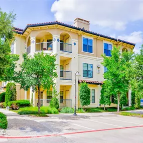 Street view of our three story, tan, apartment building surrounded by greenery