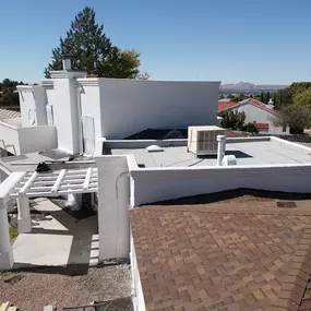 An elevated view of a multi-level home featuring both a new white, flat roof and a traditional shingled roof. The flat roof appears to be recently coated, and the property includes a pergola and chimneys.