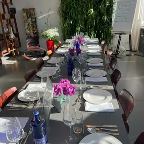 Geschlossene Gesellschaft bietet einen hell gedeckten Tisch mit weißen Tellern, Gläsern und Blumenschmuck für ein Social Dining Erlebnis in Hamburg.