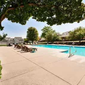 A pool surrounded by trees and chairs.