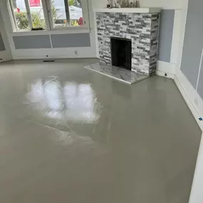 This image shows a newly installed mosaic floor in a room. The patterned blue, beige, and black tile is visible in the foreground, with an entryway leading to an unfinished room with exposed subflooring.