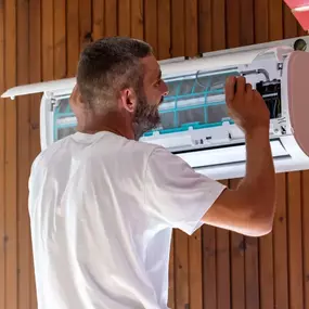 A man repairing a wall mounted air conditioner unit, representing hands-on HVAC maintenance and part replacement.