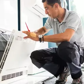 A professional technician working on a central air conditioner unit indoors, illustrating HVAC system servicing