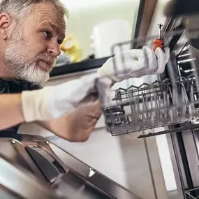 A man wearing gloves using a screwdriver to repair the interior of a dishwasher, demonstrating hands-on maintenance