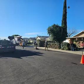 On a sunny day, workers from Clark's Tree Works are cleaning up a street with a wood chipper and a dump trailer. They are clearing branches, indicating a recent tree trimming or removal project.