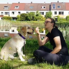 Ein ruhiger Moment der Verbindung – Mensch und Hund genießen die Natur am Wasser, umgeben von blühendem Leben.