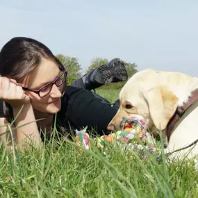 Ein Moment echter Verbindung: Eine Frau liegt entspannt mit ihrem Hund auf der Wiese. Gemeinsame Zeit, Vertrauen und spielerisches Miteinander – das ist die Basis für ein starkes Mensch-Hund-Team.