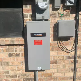 A close-up shot of a residential electrical panel installation on a red brick wall. A Generac generator disconnect switch with a prominent red 