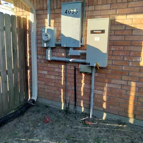 A photo showing a residential outdoor electrical setup on a red brick wall. The installation features a meter, an electrical panel with 