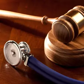 A close-up shot of a wooden gavel and a stethoscope on a dark, polished wooden surface, representing the fields of law and medicine.