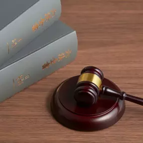 A gavel with a golden band rests on its sound block on a wooden desk, next to a stack of two gray law books.