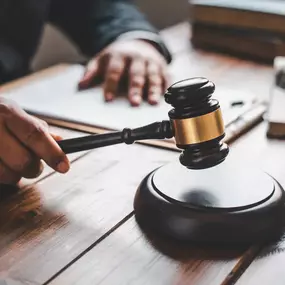 A person in a suit is holding a gavel over a sound block on a wooden desk, symbolizing a judge or lawyer preparing to make a legal decision.