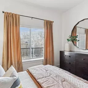 Bright bedroom at Skylark Apartments in Atlanta with large window, modern dresser, round mirror, and cozy bedding.