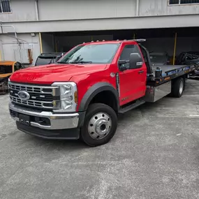A new, red Ford Super Duty flatbed tow truck is parked on a gray asphalt lot. The truck is clean and ready for service.